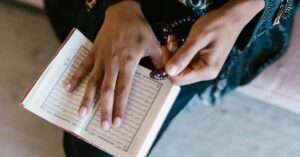 Close-up of a woman reading the Quran while holding prayer beads, focusing on spirituality and prayer.