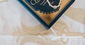 Top view of an elegant Quran and prayer beads on ornate white cloth, symbolizing Islamic faith.
