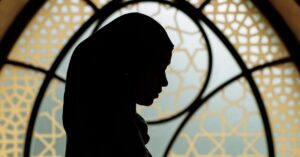Silhouette of a woman reading in front of Islamic-patterned window. Peaceful and cultural ambiance.