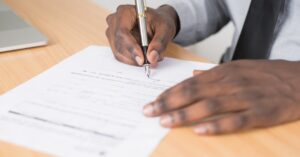 Close-up of a businessman signing a contract at an office desk.